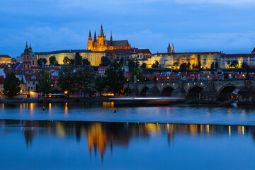Prague Castle and Charles Bridge illuminated at blue hour with reflections in Vltava River, historic cityscape of Prague, Czech Republic