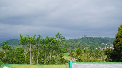 A lush, green hilly landscape with trees and a satellite dish under a dramatic, cloudy sky.