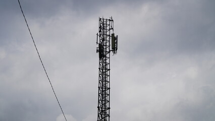 A telecommunications tower with antennas, set against a dramatic, cloudy gray sky.