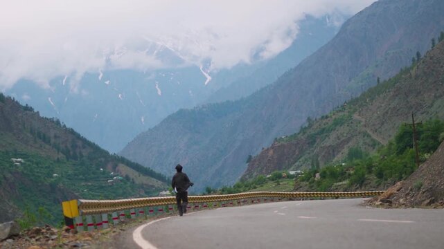 Defocused Indian man running in front of Himalayan mountain ranges covered by clouds during the monsoon season near Udaipur in Pattan Valley, Lahaul, Himachal Pradesh, India. 