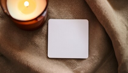 blank square sticker on cozy fabric background with candle for design mockup