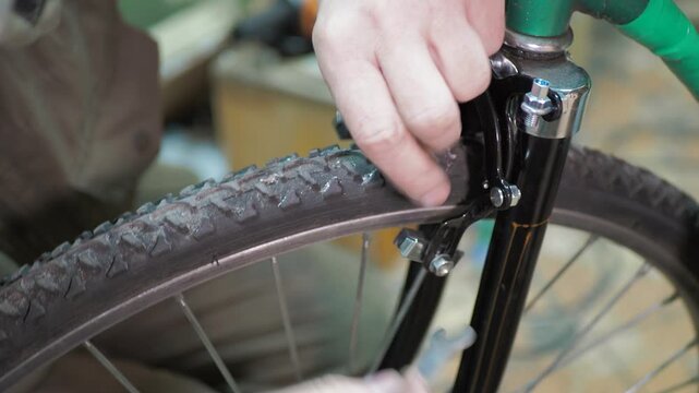 Workshop. A worker uses a wrench to install rim brakes on the front fork of an old bicycle.