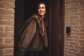 Pretty brunette long hair woman in casual outfit going out of house. Girl wear green trench coat or...