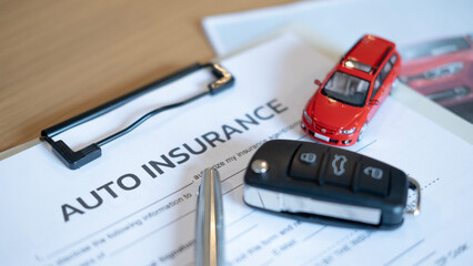 Car insurance form with pen black key and miniature red vehicle showing legal contract safety...