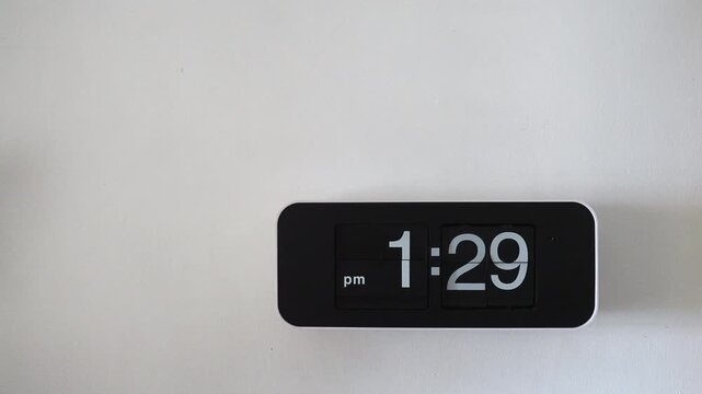 Wall clock flip with black face hanging on a white wall background.