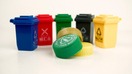 Plastic bottle caps in focus with garbage bins in the background representing the global micro plastics pollution crisis and recycling challenges. Conceptual photo.