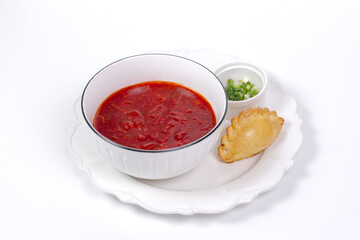 Traditional borscht in a white bowl with a pie and chopped herbs.