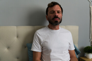 Lonely Latin man sitting on bed after breakup in bedroom