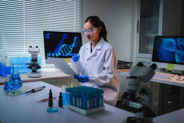 Female scientist in a lab coat and safety glasses is reading genetic research data, with DNA helixes showing on computer screens