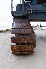 A close-up of an excavator track. A close-up of a part of a construction excavator, a tracked vehicle. Repair work on a beach by the sea. Equipment at a construction site. 
