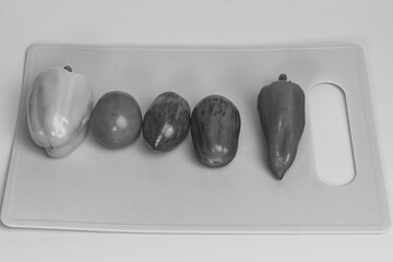 Black and white overhead shot of a fresh vegetable assortment—two bell peppers and three tomatoes—on a cutting board.