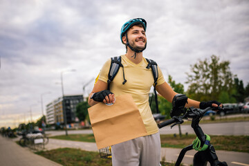 Courier rides bicycle in urban streets holding food package in hand, concept of fast delivery, urban transport, courier job, modern city lifestyle.