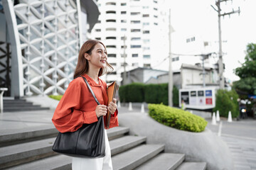 Fototapeta premium A beautiful Asian businesswoman carrying binders and standing outside of the corporate building.
