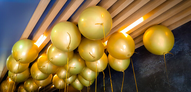 Golden balloons with ribbons floating to a wooden slatted ceiling, creating a festive atmosphere.