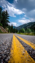 A paved highway meanders through a scenic mountain valley, lined with towering evergreens and highlighted by vibrant yellow center lines.