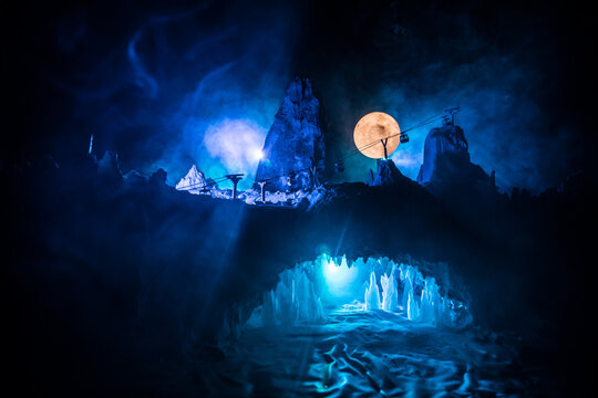 Surreal landscape with people exploring mysterious ice grotto cave. Outdoor adventure. Family exploring huge icy cave, dark majestic landscape. Magical silhouettes on background of illuminated ice