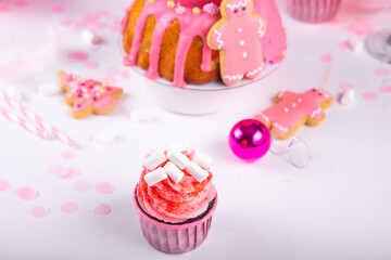 Pink Christmas cupcake with marshmallow and traditional fruit cake on the background. Winter homemade baking. Festive table.