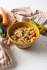 Bowl of cous cous with fresh vegetables on a white background.