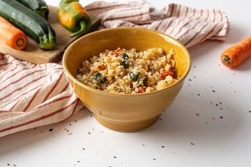 Bowl of cous cous with fresh vegetables on a white background.