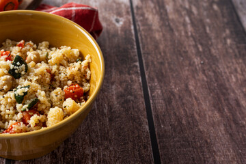 Rustic bowl of couscous with vegetables on dark wooden table