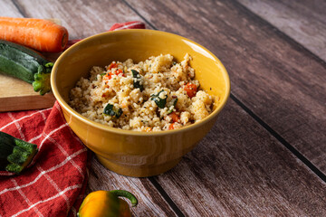 Rustic bowl of couscous with vegetables on dark wooden table
