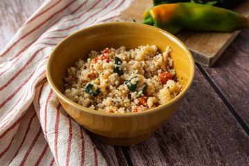 Rustic bowl of couscous with carrots, bell peppers, and zucchini on wooden table, styled with fresh vegetables. Ideal for concepts related to healthy eating, vegetarian diet, or Mediterranean cuisine.