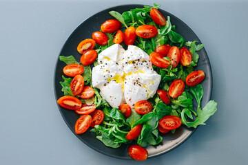 Fresh salad featuring poached eggs, cherry tomatoes, and leafy greens, beautifully arranged on a black plate, showcasing vibrant colors and healthy ingredients for a nutritious meal