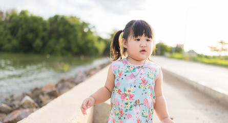 An Asian kindergarten girl stands outdoors and smiles happily while watching the sunset,Happy baby Asian girl smiling. little girl running and smiling at sunset happy baby girl smiling. 