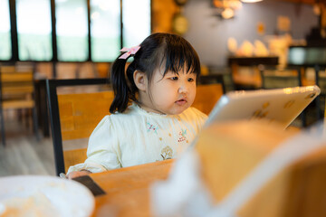 A cute little Asian girl is eating in a restaurant,Asian child cute or kid girl smile holding fork...