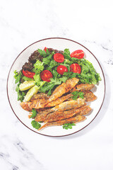 Fried crispy mullet fish, with fresh salad, on a plate with lime, no people,