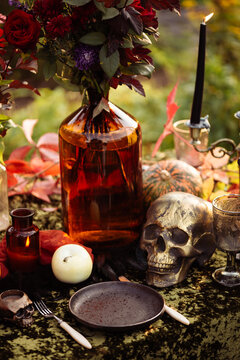 Fall themed holiday table setting for a seasonal party, glasses, pumpkins, candles, field flowers. Halloween table in the garden with scull and autumn flowers