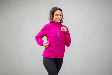Smiling woman jogging in pink jacket and black leggings outside