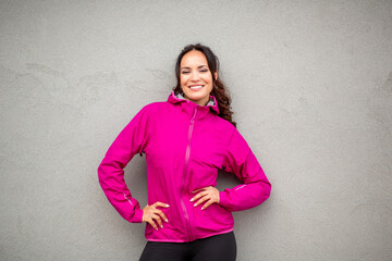 Happy woman posing in pink windbreaker against gray wall