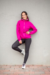 Smiling woman in pink sports jacket posing against gray wall © Paula