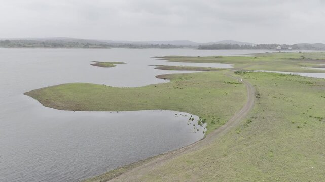 Aerial view of a curved path on Chacha Kota island, Banswara, Rajasthan during monsoon, surrounded by lush green landscape, water, and distant hills and islands.