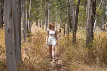 Young woman, beautiful, blonde, wearing a floral dress, relaxed and calm, walking among the trees, in connection with nature and ecology, in an outdoor park. Concept of beauty, youth, millennial.