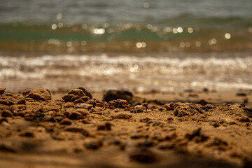 Close-up of sandy beach with rocks and blurred ocean waves in the background
