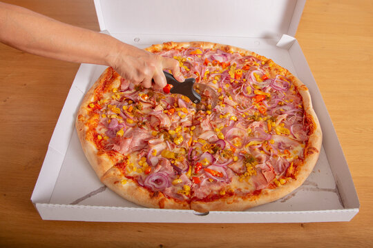 Frische Pizza im Lieferkarton, von Hand aufgeschnitten mit Pizzaroller, leckeres Fast-Food-Motiv f&uuml;r Gastronomie, Lieferservice, italienische K&uuml;che, Werbung und Foodfotografie