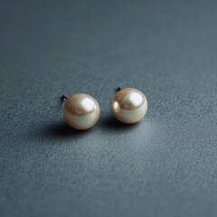 Elegant golden pearl stud earrings on a dark grey textured background.
