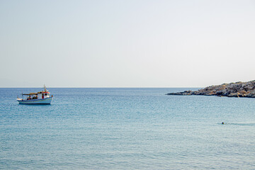 Sailboats anchored on calm blue sea near rocky shore

