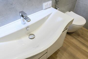 Modern bathroom with a white sink, chrome faucet, and toilet. Clean lines and neutral tones