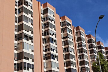 Fototapeta premium Modern residential high-rise building in Seville, Spain, featuring geometric balconies, vertical lines, and reflective windows under a clear blue sky, capturing contemporary urban architecture