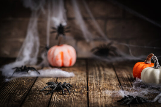 A spooky Halloween setup featuring fake spiders, pumpkins, and cobwebs on a rustic wooden table. Ideal for festive seasonal decor themes.