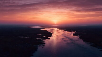Fototapeta premium Aerial view of a wide river delta at sunset with winding channels and an orange glow