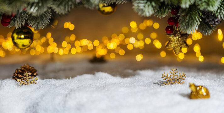 Christmas Holiday background with snow, fir tree and decorations with christmas light behind. Christmas golden balls on a winter festive background.