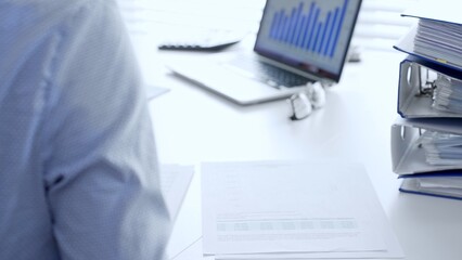 Corporate professionals reviewing financial documents, working collaboratively at white desk with blue folder stack, highlighting teamwork and business productivity. Audit and taxes in business