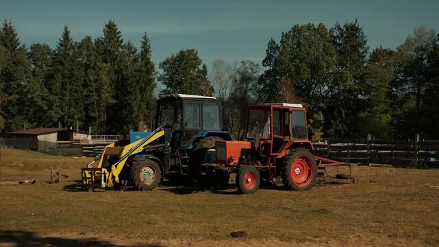 Two tractors parked in clearing next to cattle pen with wooden fence