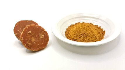 two pieces of natural brown palm sugar or javanese sugar in powder on white plate and in semicircular shapes form isolated on white background