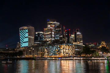 Fototapeta premium The skyscrapers of london's financial district Bank, stand tall along the river thames, casting a colorful reflection of city lights on the water at night as night falls