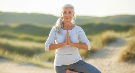 A graceful senior woman with grey hair in a tranquil yoga pose, standing on one leg with hands in prayer position on a sandy beach. Symbolizes healthy aging, mindfulness, and peace.